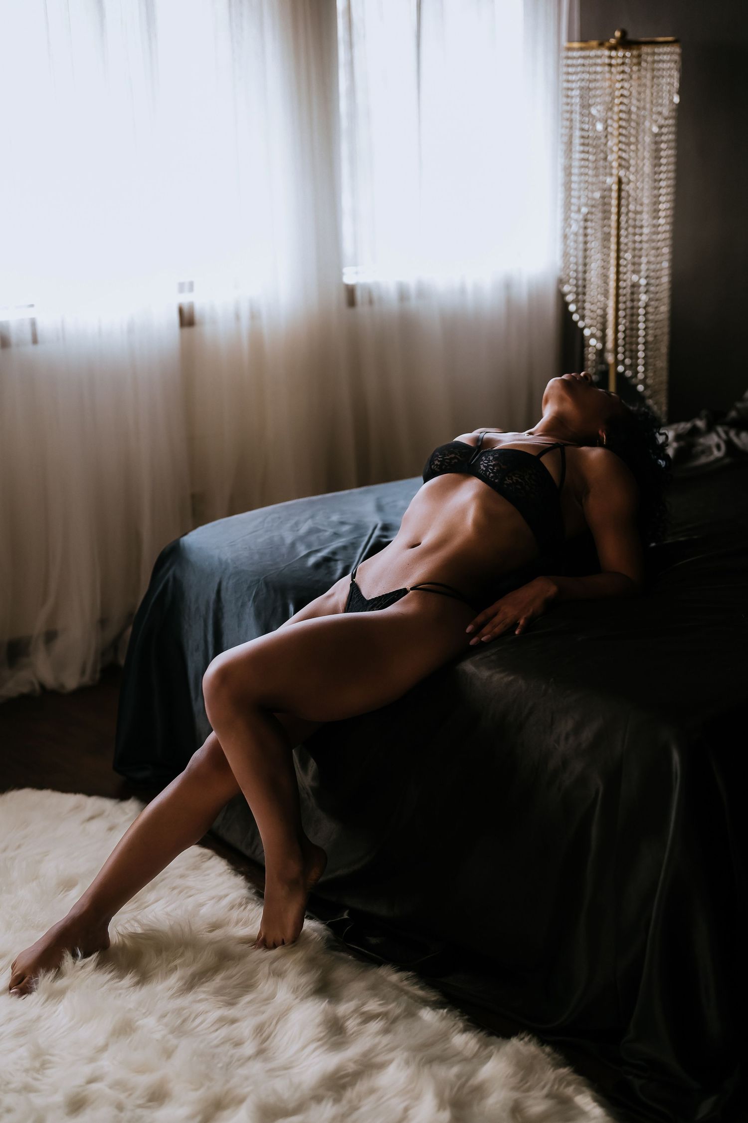 Artistic boudoir photo series showing person in black lingerie reclining on white faux fur rug in moody lighting.