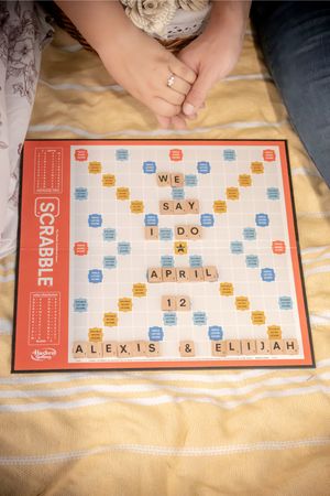 Scrabble board displaying a wedding announcement with tiles spelling We Say I Do April 12 Alexis and Elijah.