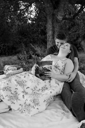 Black and white photo of a couple laughing together on a picnic blanket under a tree.