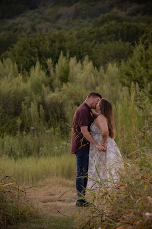 Couple sharing a romantic kiss in a lush green meadow, man in burgundy shirt and woman in floral dress.