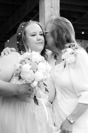 Black and white wedding photo showing tender moment as older woman kisses bride holding white rose bouquet.