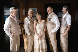 Wedding party wearing cream and ivory colored attire pose together inside rustic wooden interior.