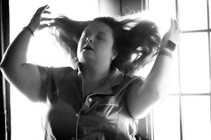 Dramatic black and white portrait shows someone reaching up in front of sunlit window.