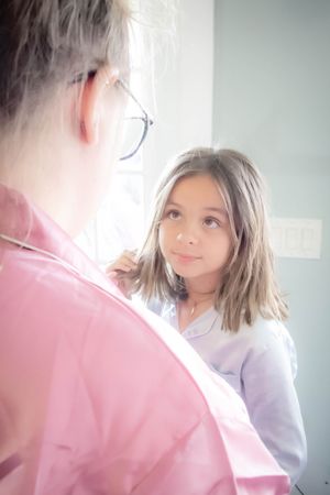 A young patient looks up attentively while speaking with a medical professional wearing a pink coat in a clinical setting.