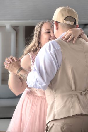 A couple shares an intimate dance moment, with the woman in a pink dress and the man wearing a tan vest.