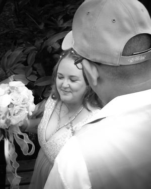 A romantic black and white wedding moment as the couple shares an intimate scene with white flowers outdoors.