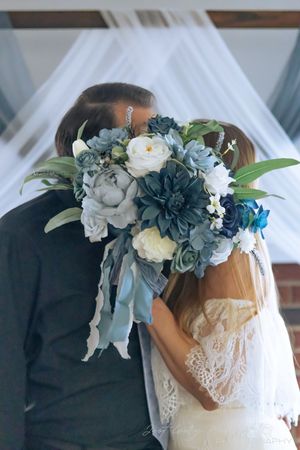 Delicate floral crown featuring dusty blue succulents, white roses and greenery adorns a lace wedding dress.