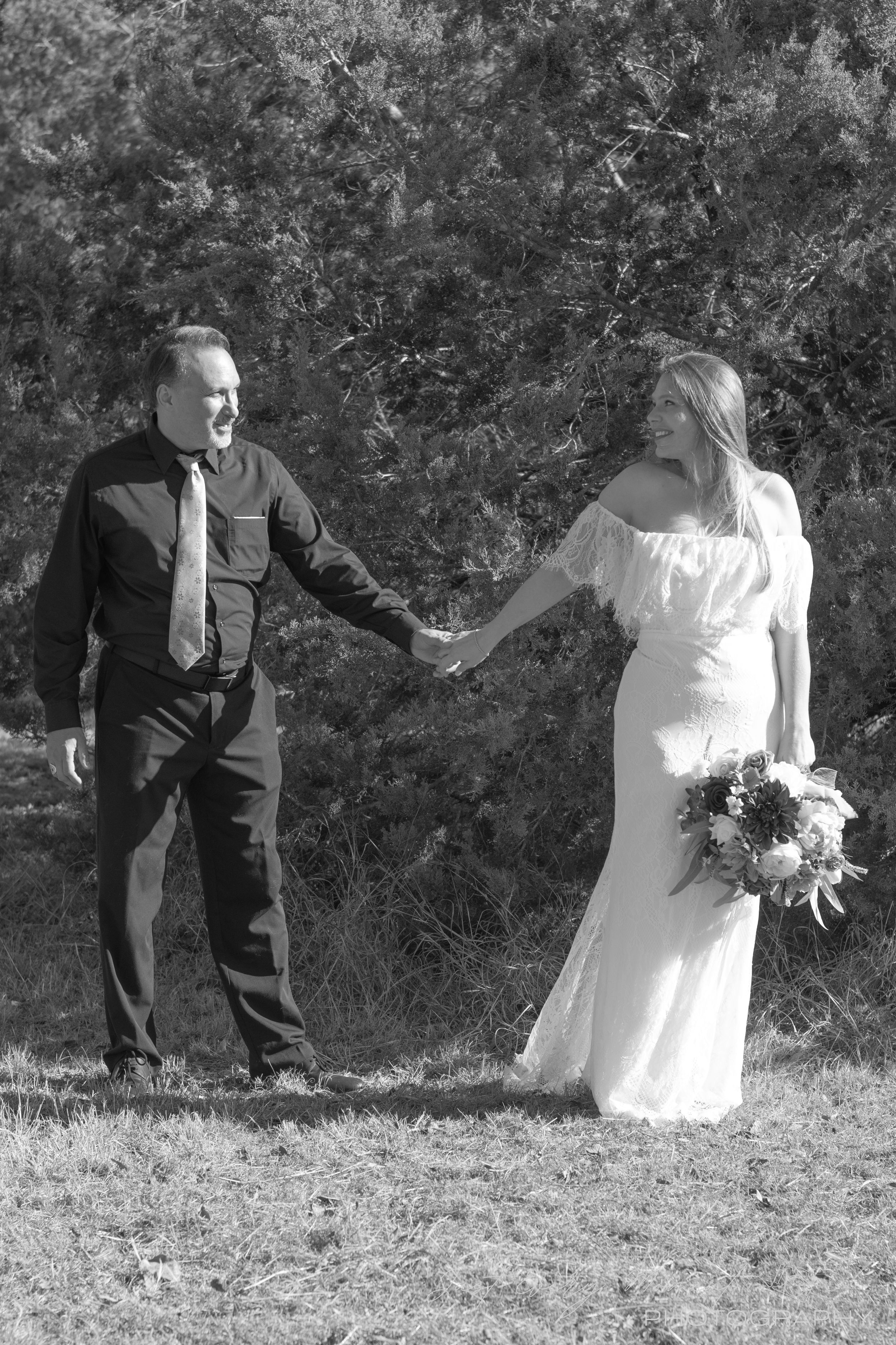 A black and white wedding photo showing a couple holding hands outdoors with trees in the background.