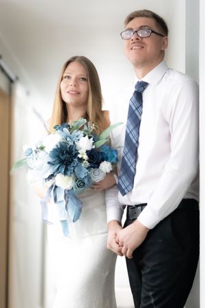 A couple in wedding attire pose together, with the bride holding a blue and white floral bouquet.