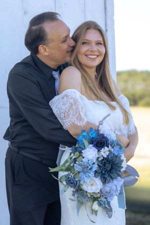 A couple shares a romantic moment at their wedding, with the bride holding a stunning blue and white floral bouquet.