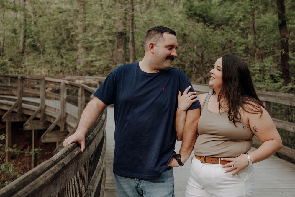 A couple shares an intimate moment on a rustic wooden bridge in a natural setting.