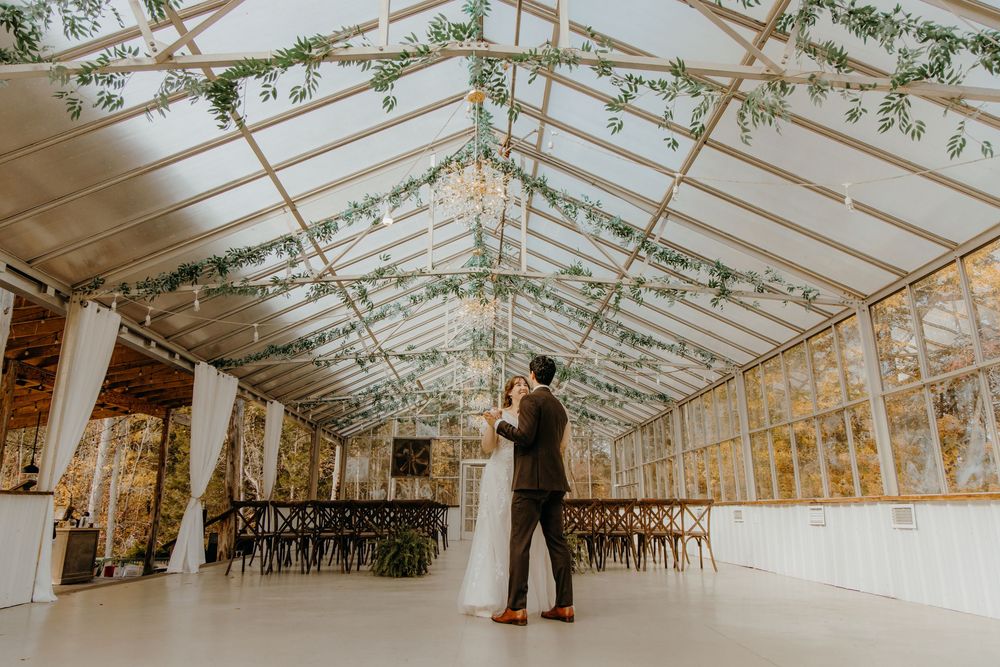 Elegant greenhouse wedding venue with glass ceiling, wooden beams, and natural light filtering through leafy decor.