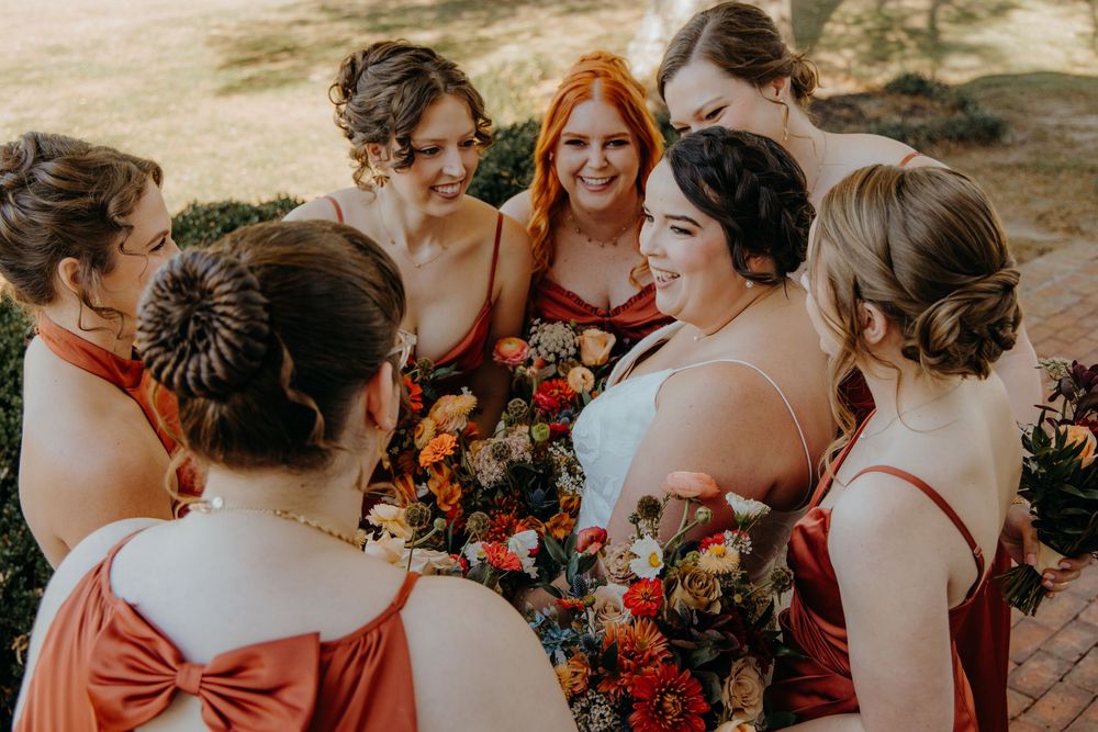 A bridal party wearing burgundy dresses gathers together for candid moments in an outdoor setting.