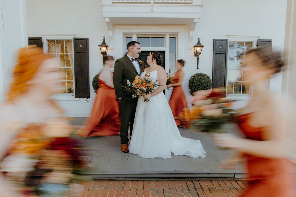 A blurred motion sequence of people in formal attire walking past a white building with lanterns at dusk.