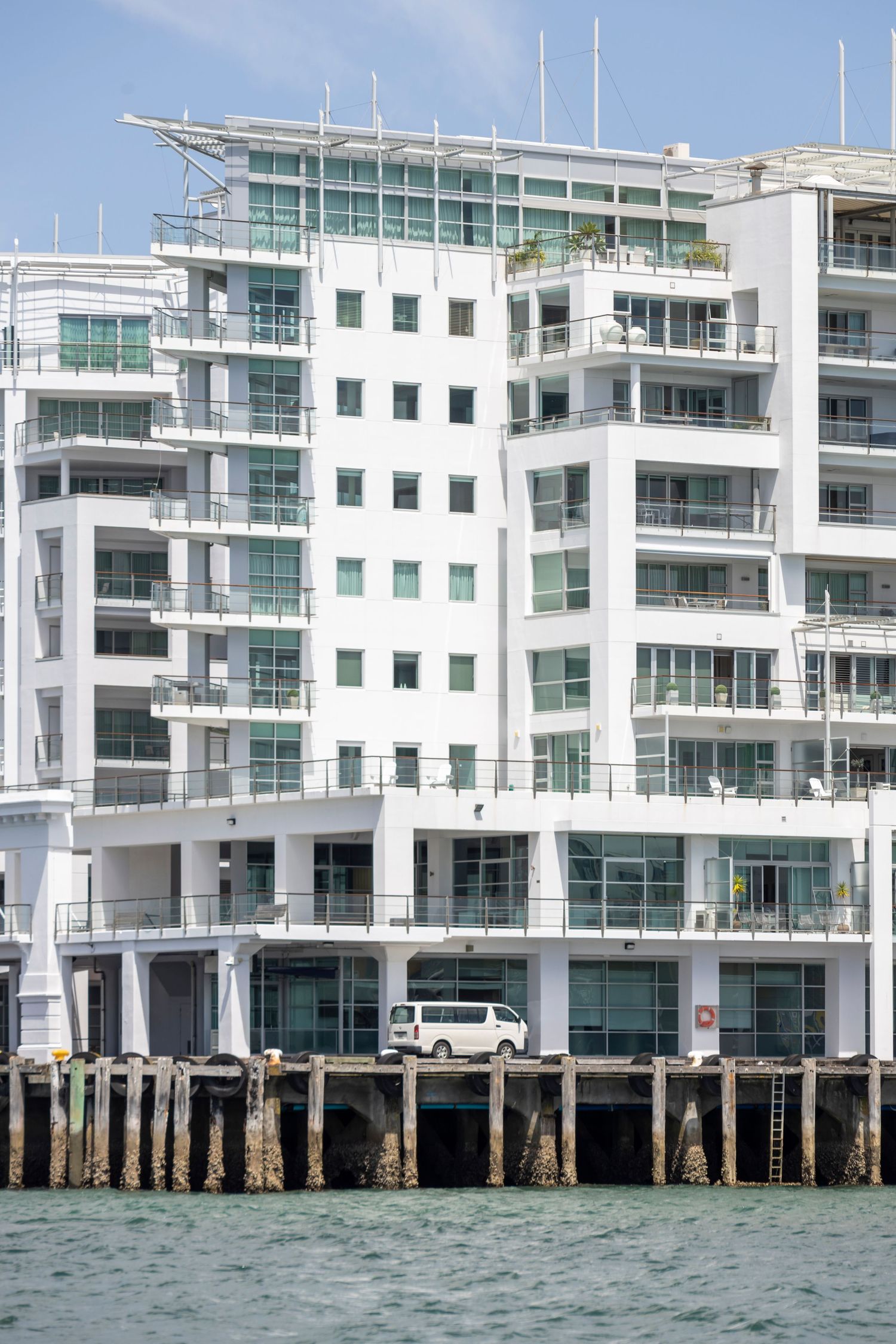 White waterfront apartment block with balconies and glass, perched on stilts above the sea.