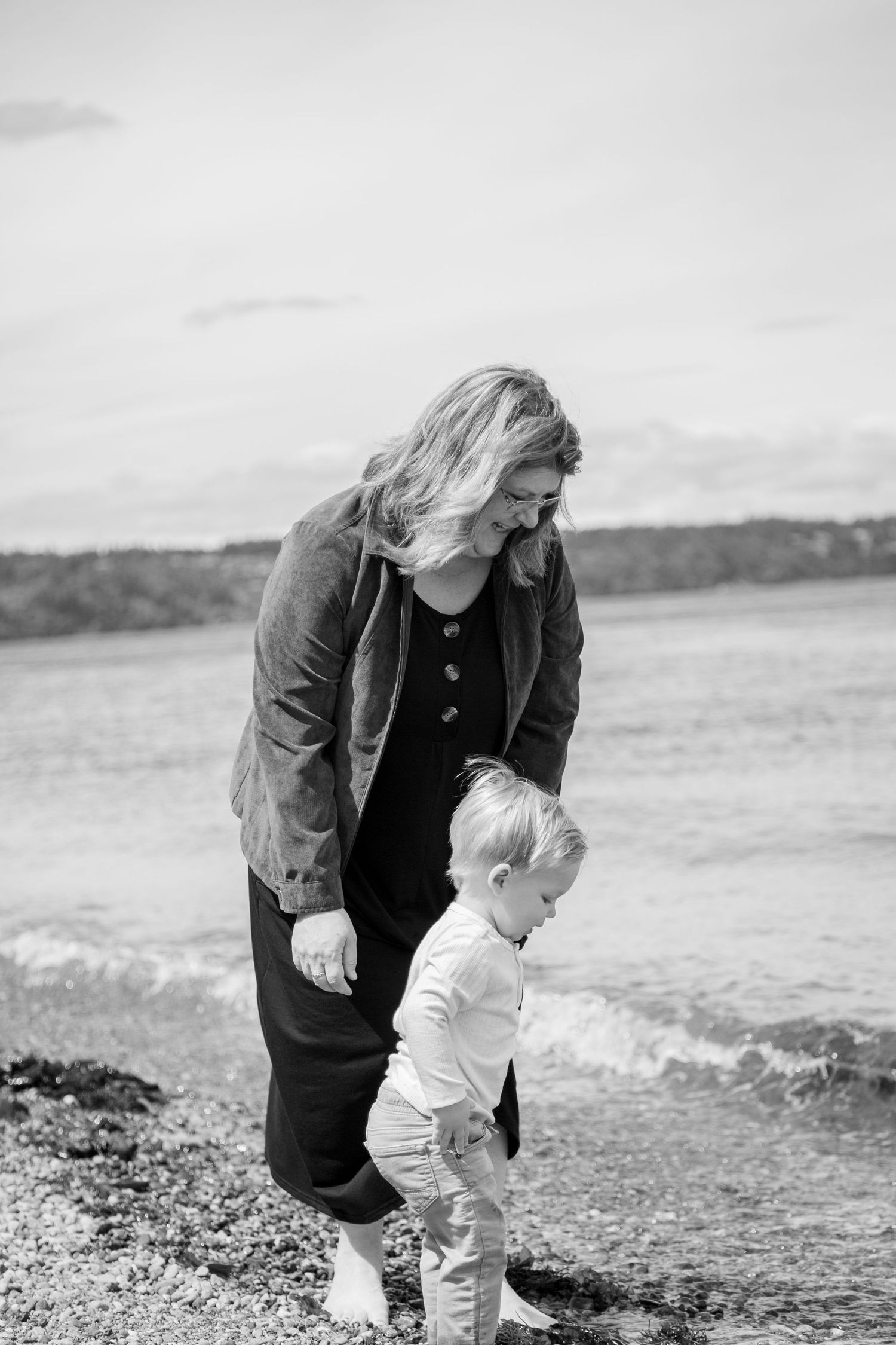 Black and white coastal photo showing caring moment between two people walking along rocky shoreline.