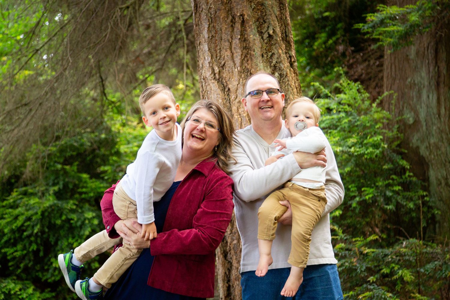 A cheerful family poses together in front of large redwood trees in a lush forest setting.