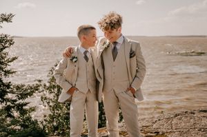 Wedding party in beige suits poses for photos on a beach at sunset while waves crash in the background.