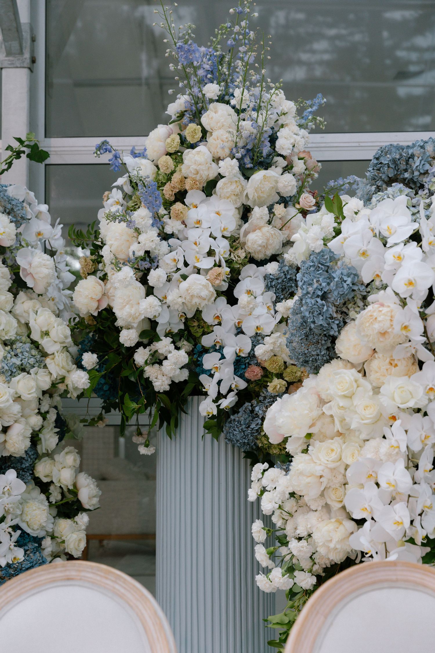 Elegant white floral arrangements with orchids and blue accents adorn classic white columns in a luxurious wedding setup.
