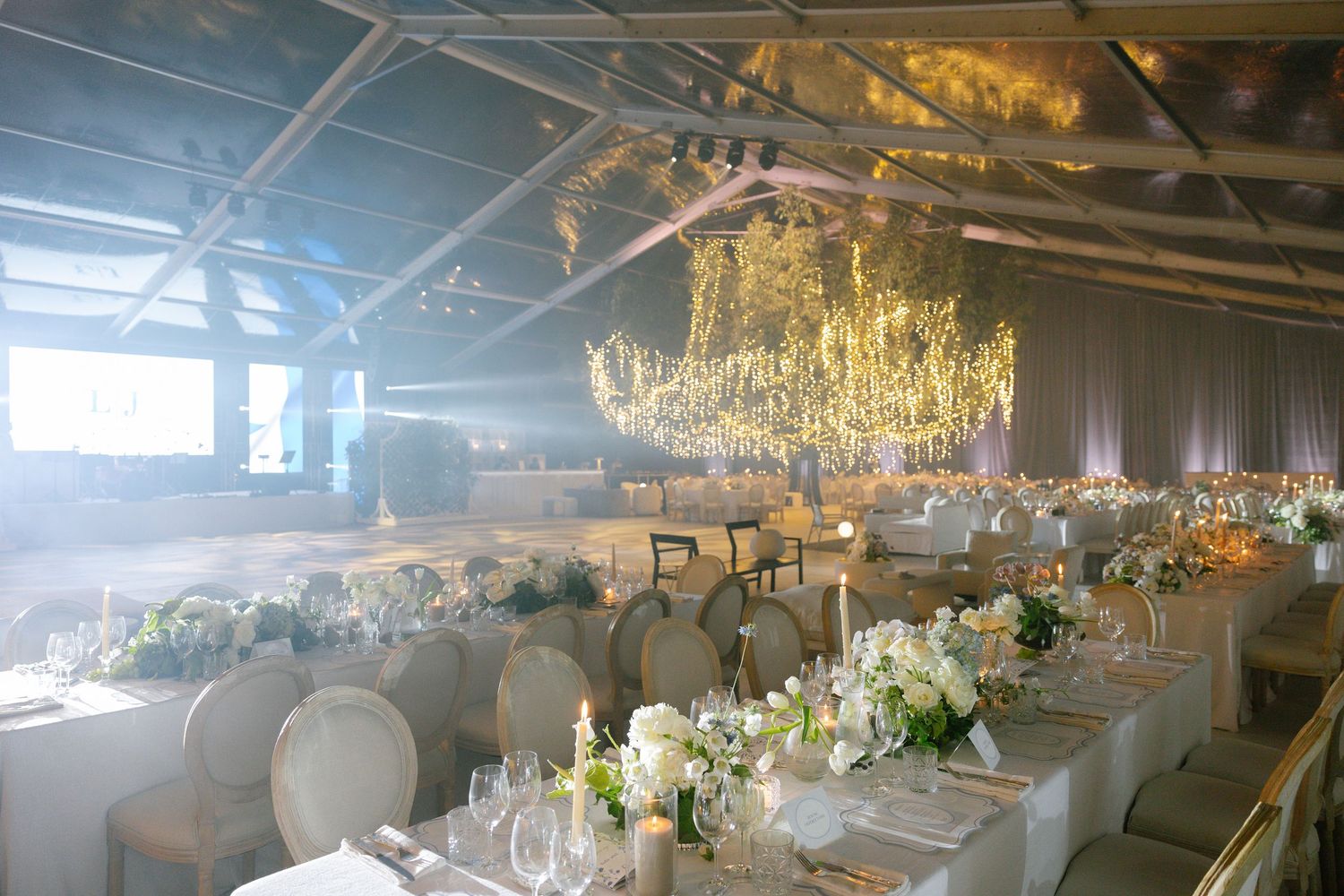 Elegant wedding reception venue with crystal chandeliers and white table settings in a modern industrial space.