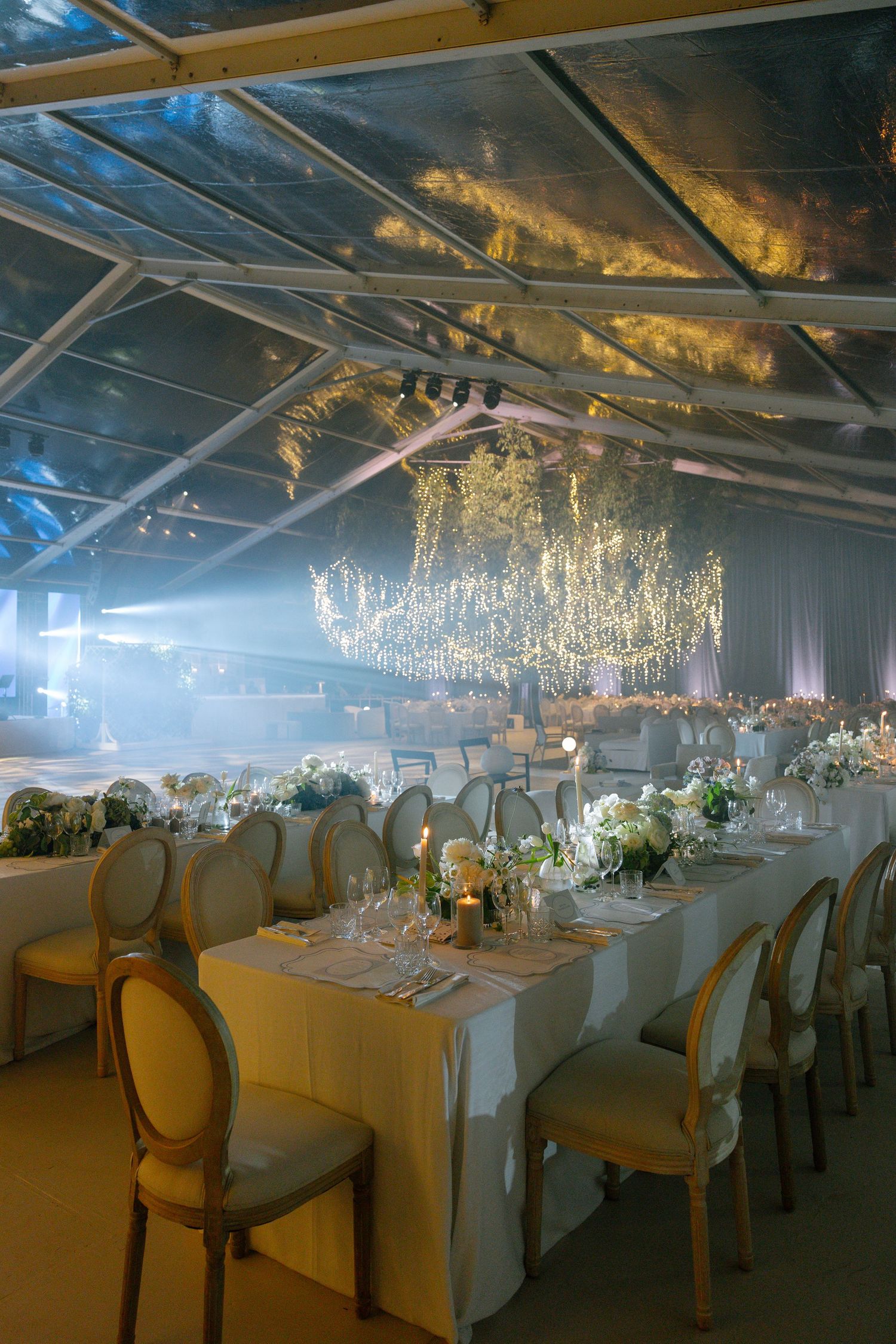 Opulent reception hall with crystal chandeliers and white-clothed tables set for an elegant wedding celebration.