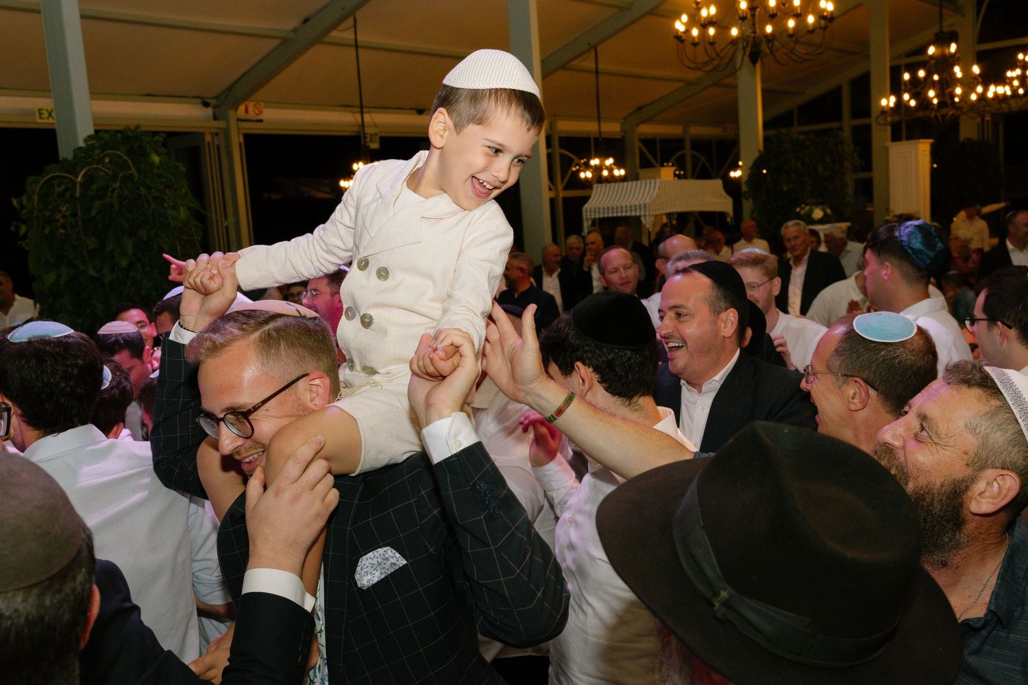 Wedding guests dancing and celebrating together on a crowded dance floor under warm lighting.