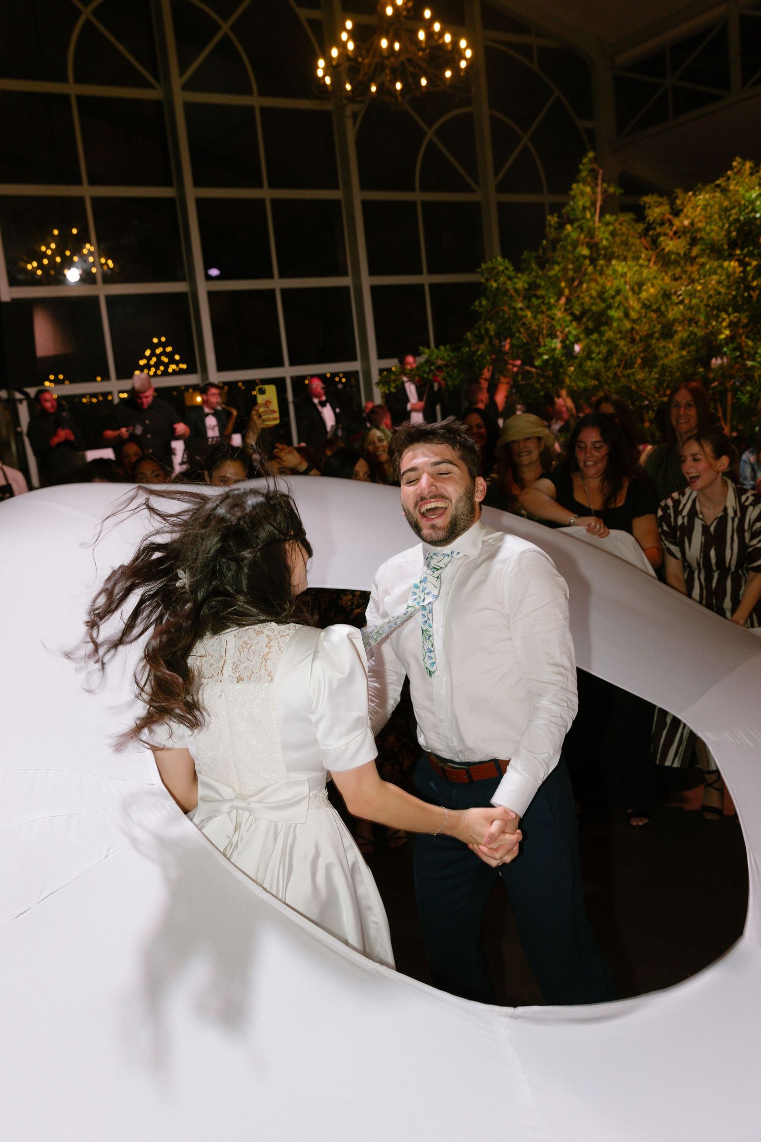 Wedding couple and guests dancing energetically in a circle during a traditional celebration dance.