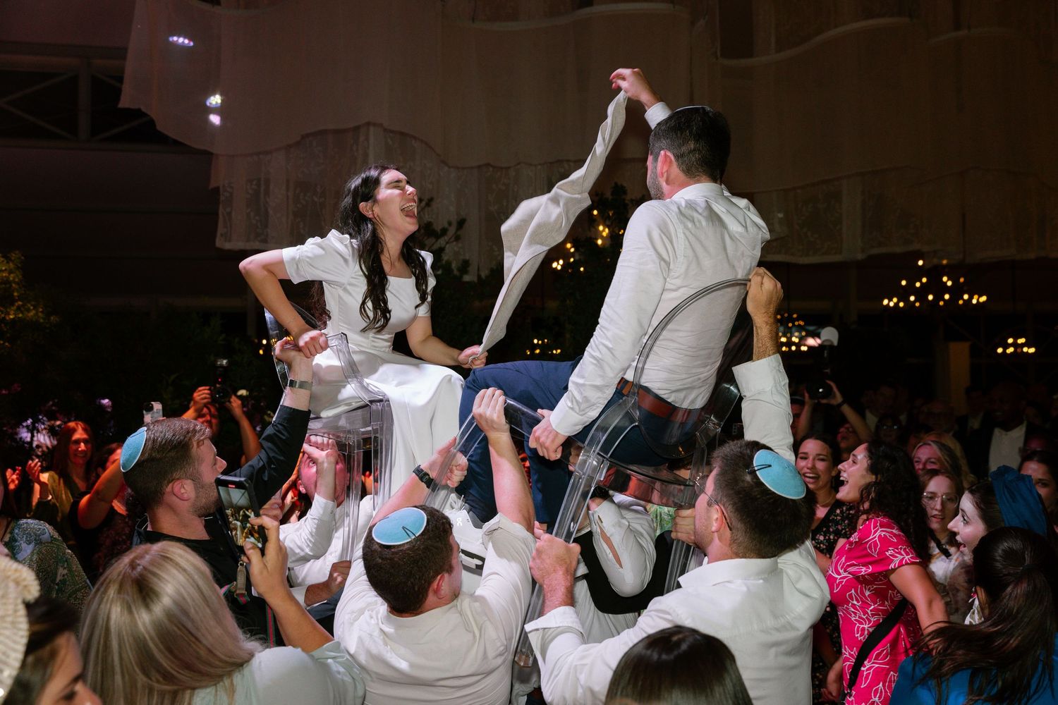 Wedding guests dancing and celebrating energetically on a crowded dance floor at a reception.