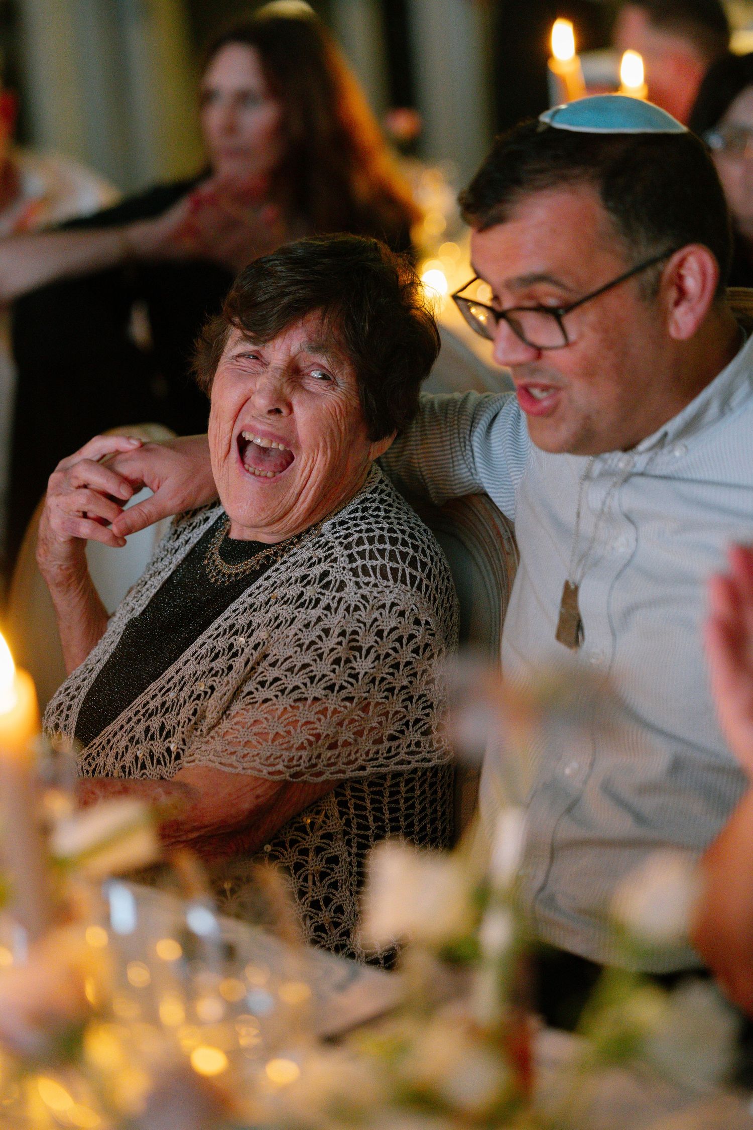 Candid moment of guests laughing during an evening dinner reception with warm candlelight.