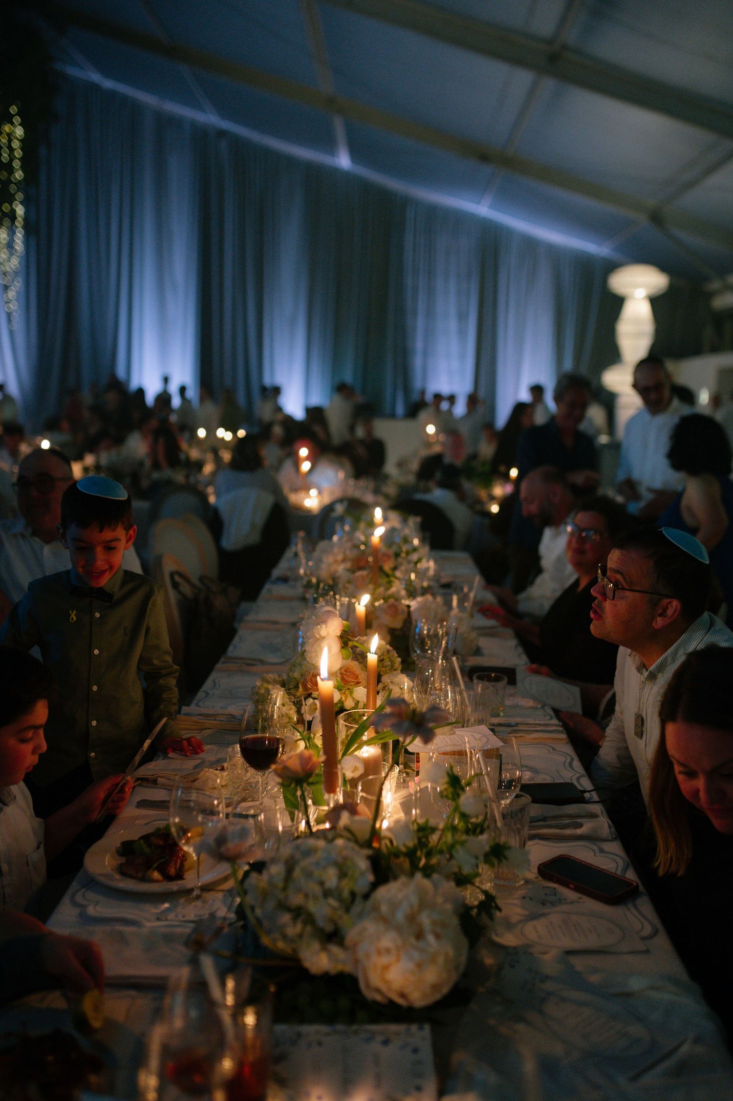 An elegant candlelit wedding reception dinner table with floral centerpieces in a tented venue.