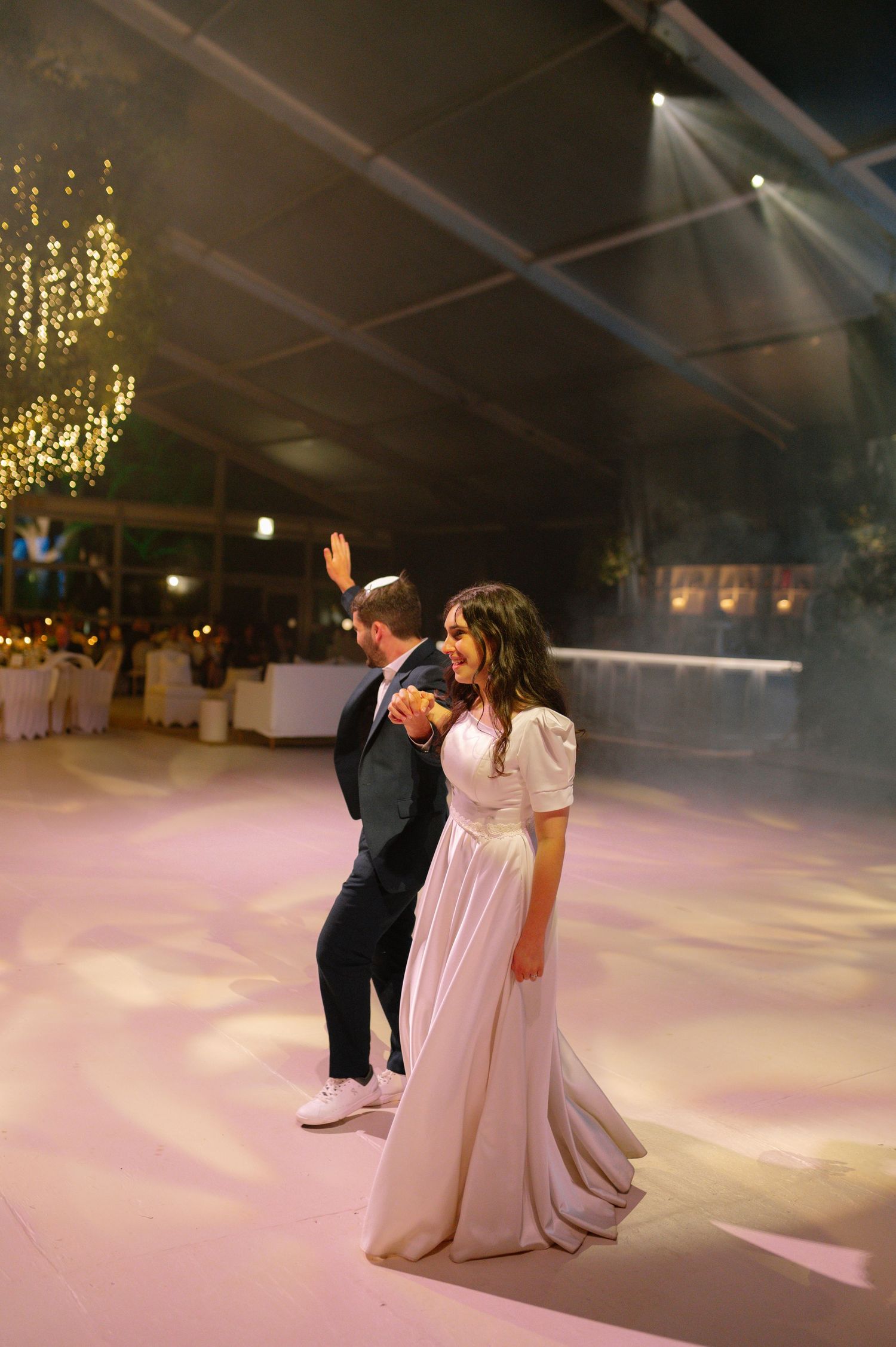 Couple dancing on illuminated pink dance floor under hanging lights at wedding reception.
