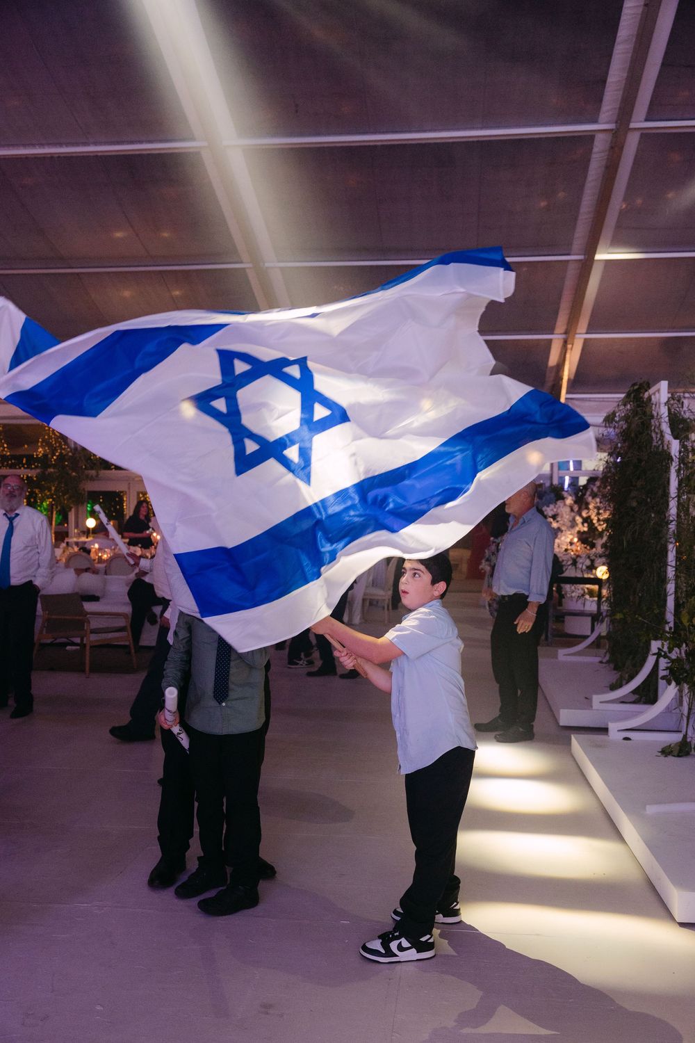 People waving Israeli flags in an indoor space with dramatic lighting and reflective floors.