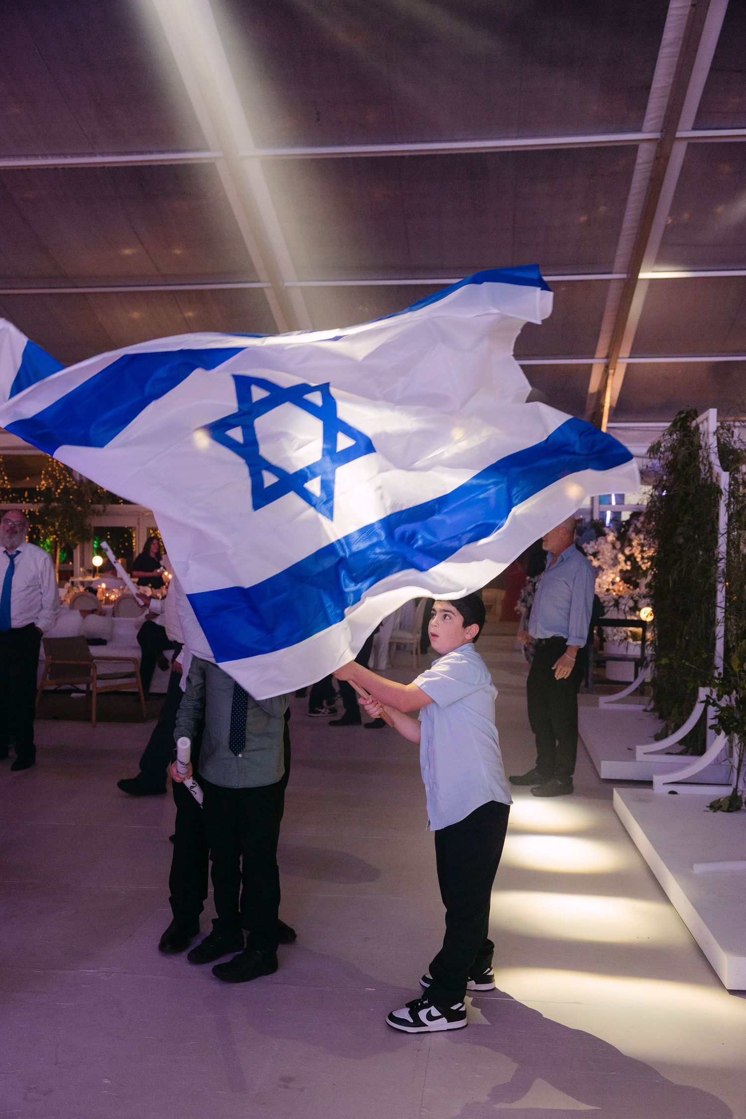 People waving Israeli flags in an indoor space with dramatic lighting and reflective floors.
