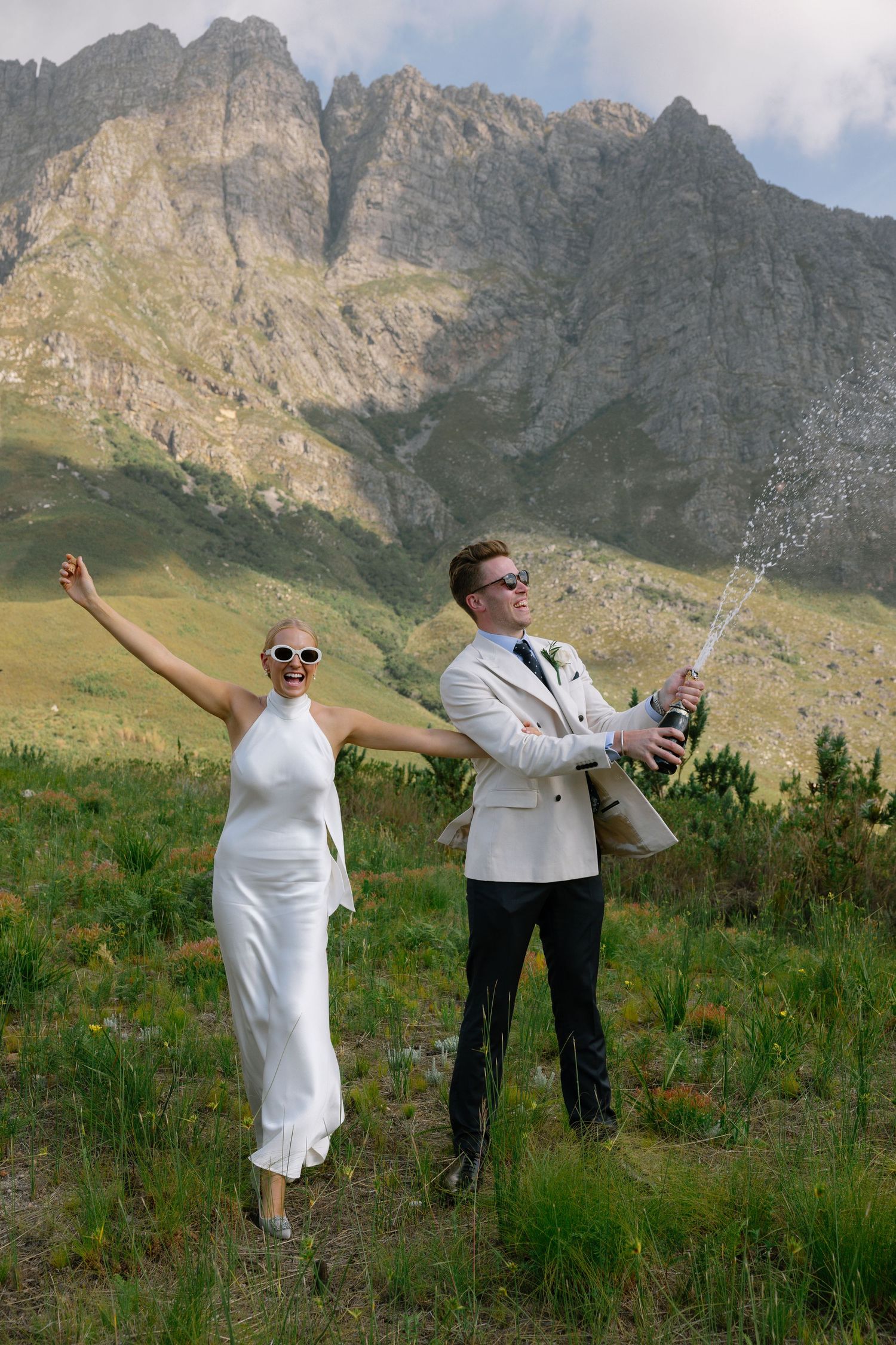 A couple poses playfully in a series of photos against a dramatic mountain backdrop in an alpine meadow.