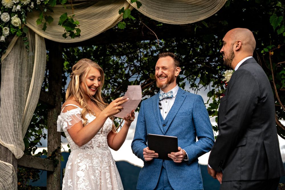 Wedding ceremony taking place outdoors under white fabric draping with guests seated in chairs on a sunny day.