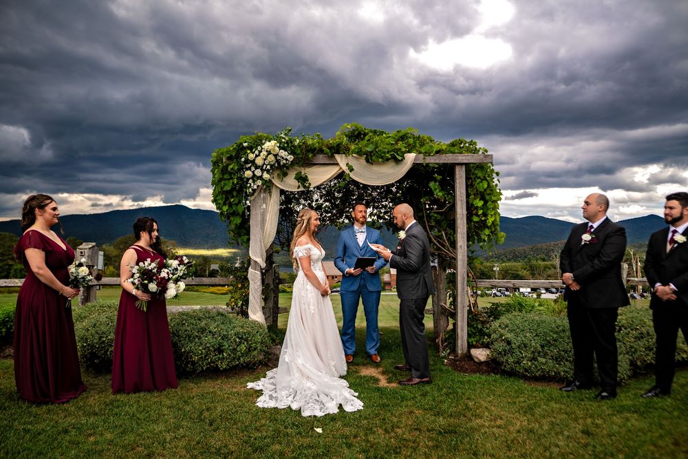 Wedding party stands in a dramatic mountain landscape under moody storm clouds during an outdoor ceremony.