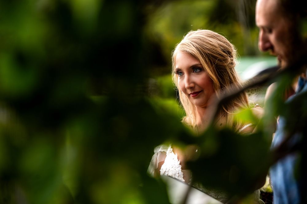 A couple shares a joyful moment during their wedding celebration outdoors with green foliage in the background.