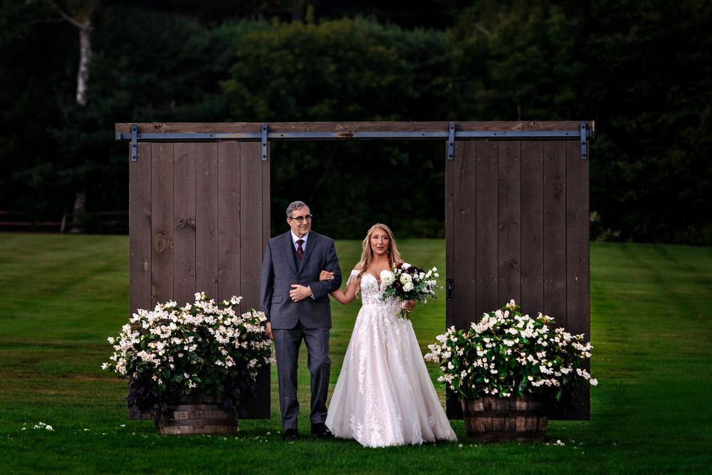 Rustic barn doors serve as a romantic backdrop for a wedding couple posing in a lush outdoor garden setting.