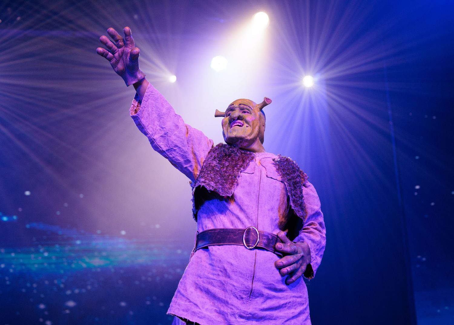 Stage performer in flowing costume illuminated by dramatic purple spotlights during an emotional performance.