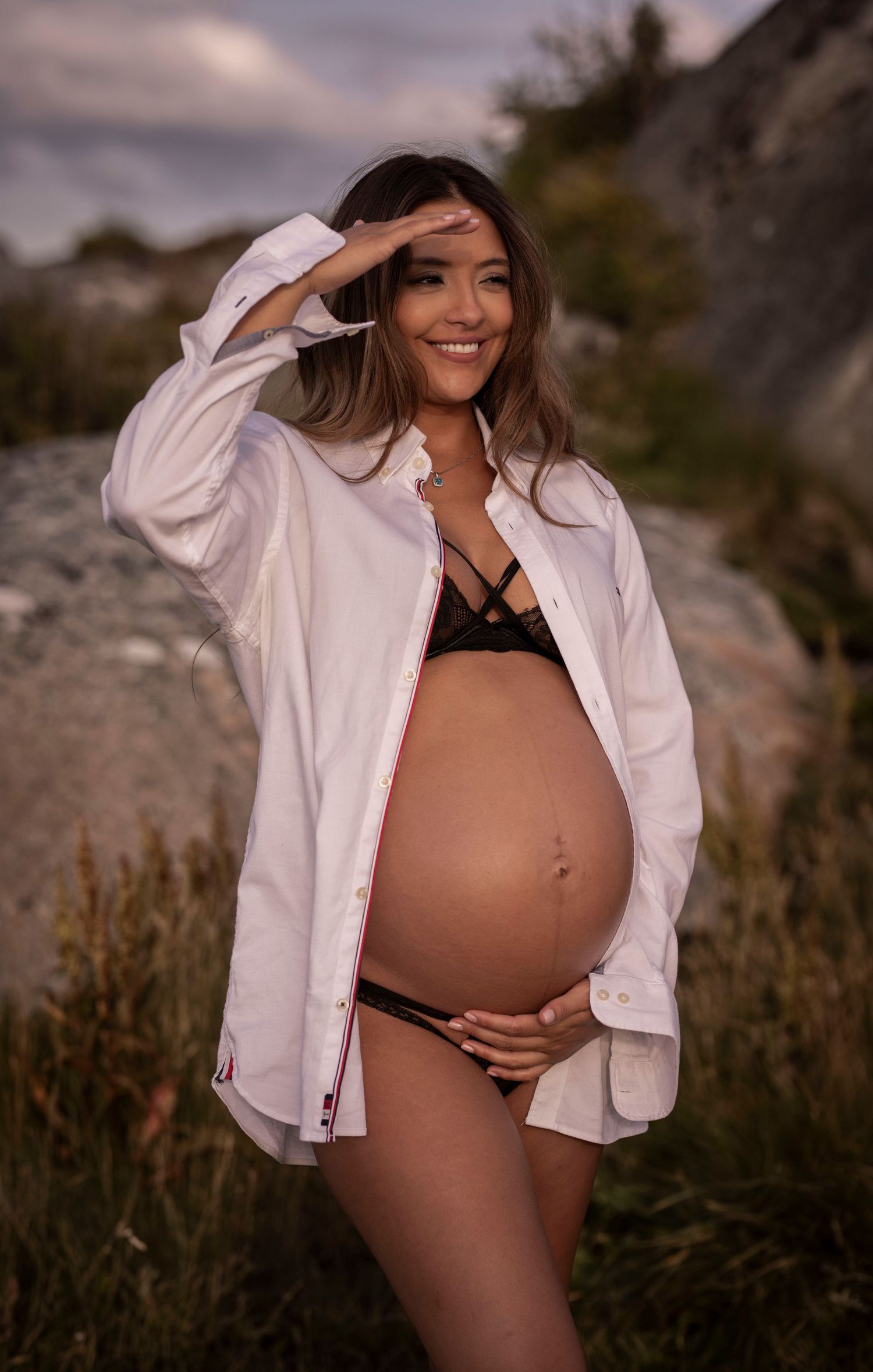gravid kvinna står och kollar utåt, hon har en vit skjorta på sig. i bakgrunden syns klippor.