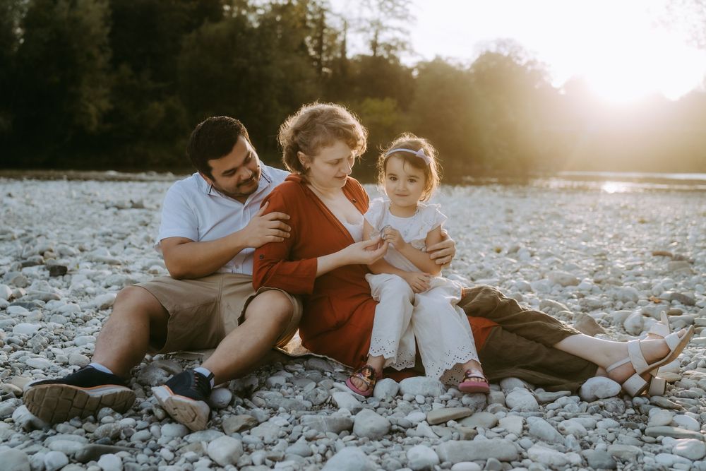 Family relaxing together on rocky riverbank during golden hour sunset.