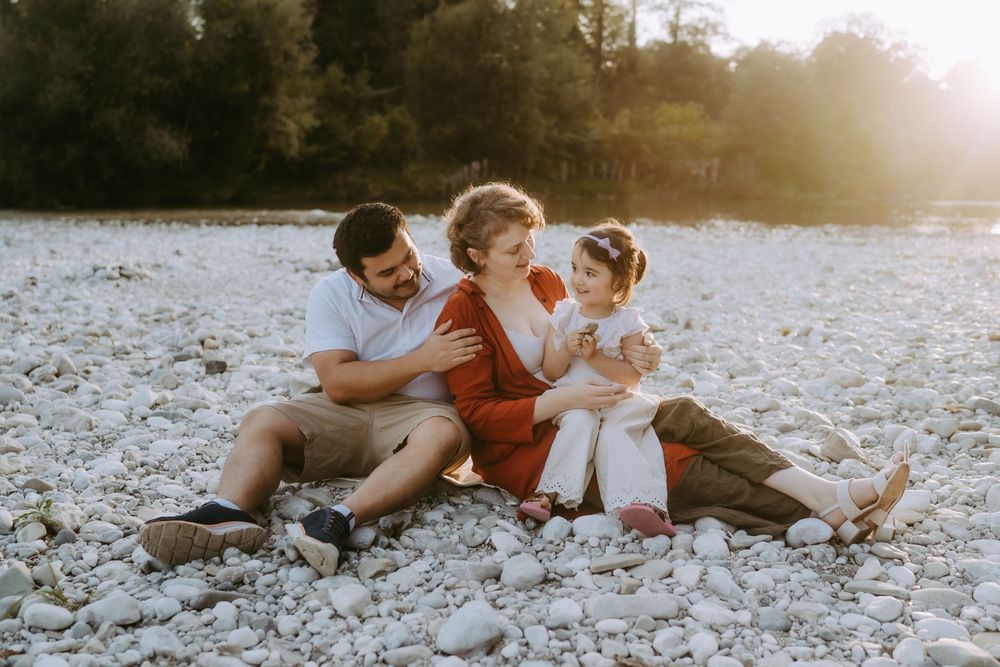 Family sitting together on rocky beach during sunset with trees in background.