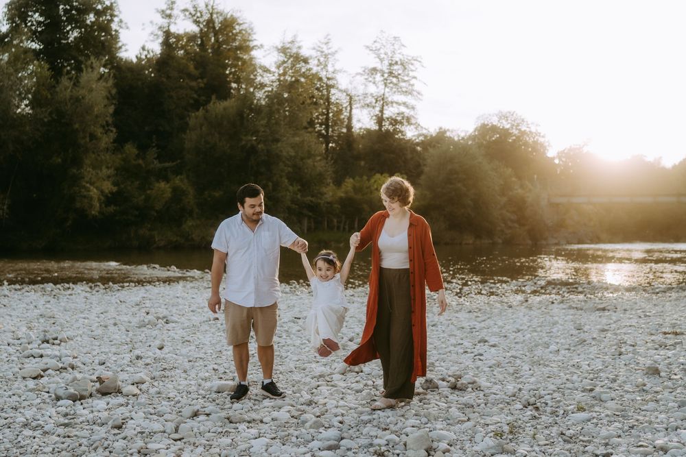 Family holding hands while standing on rocky beach during golden hour.