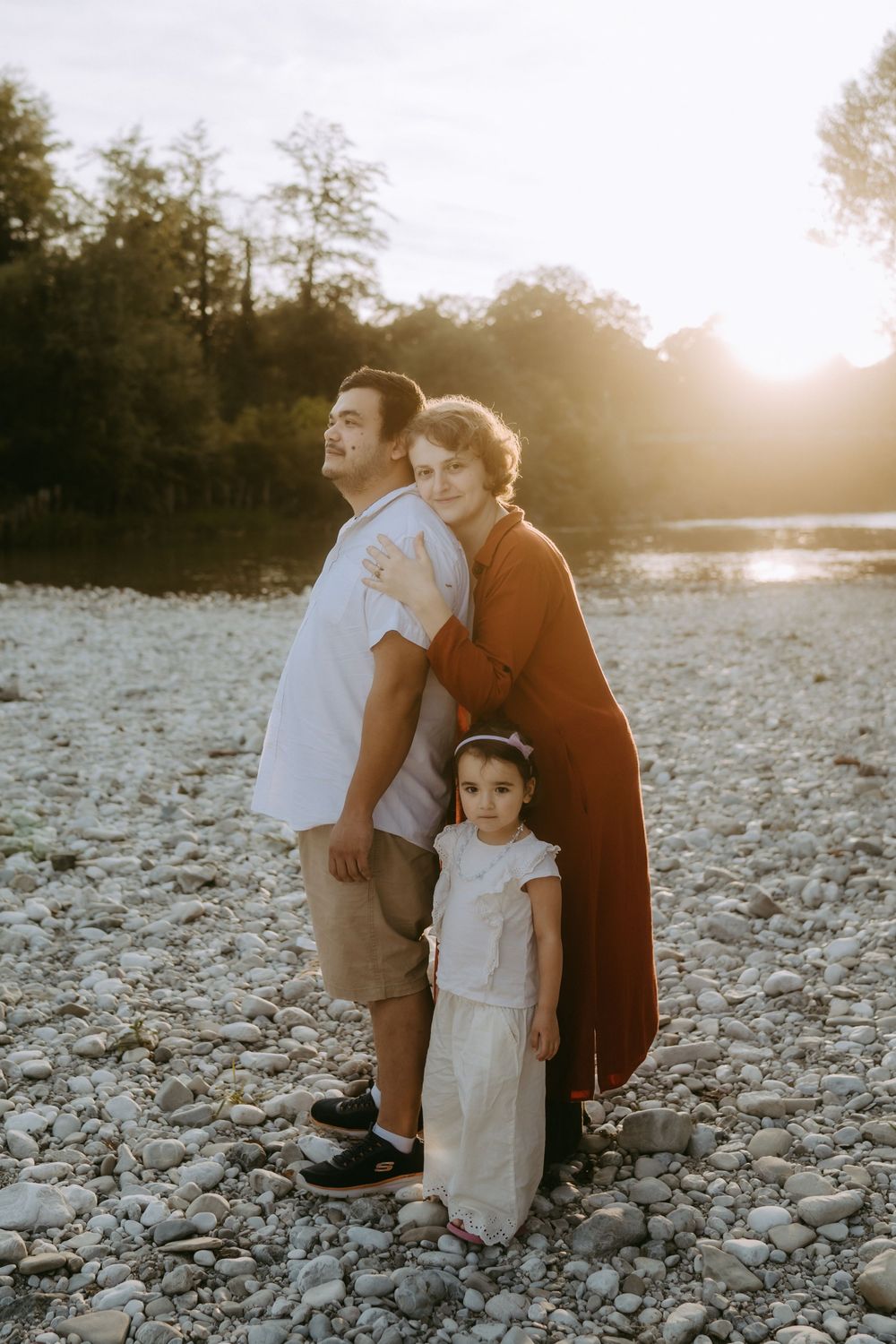 Family portrait on rocky beach with sunset backlighting through trees.