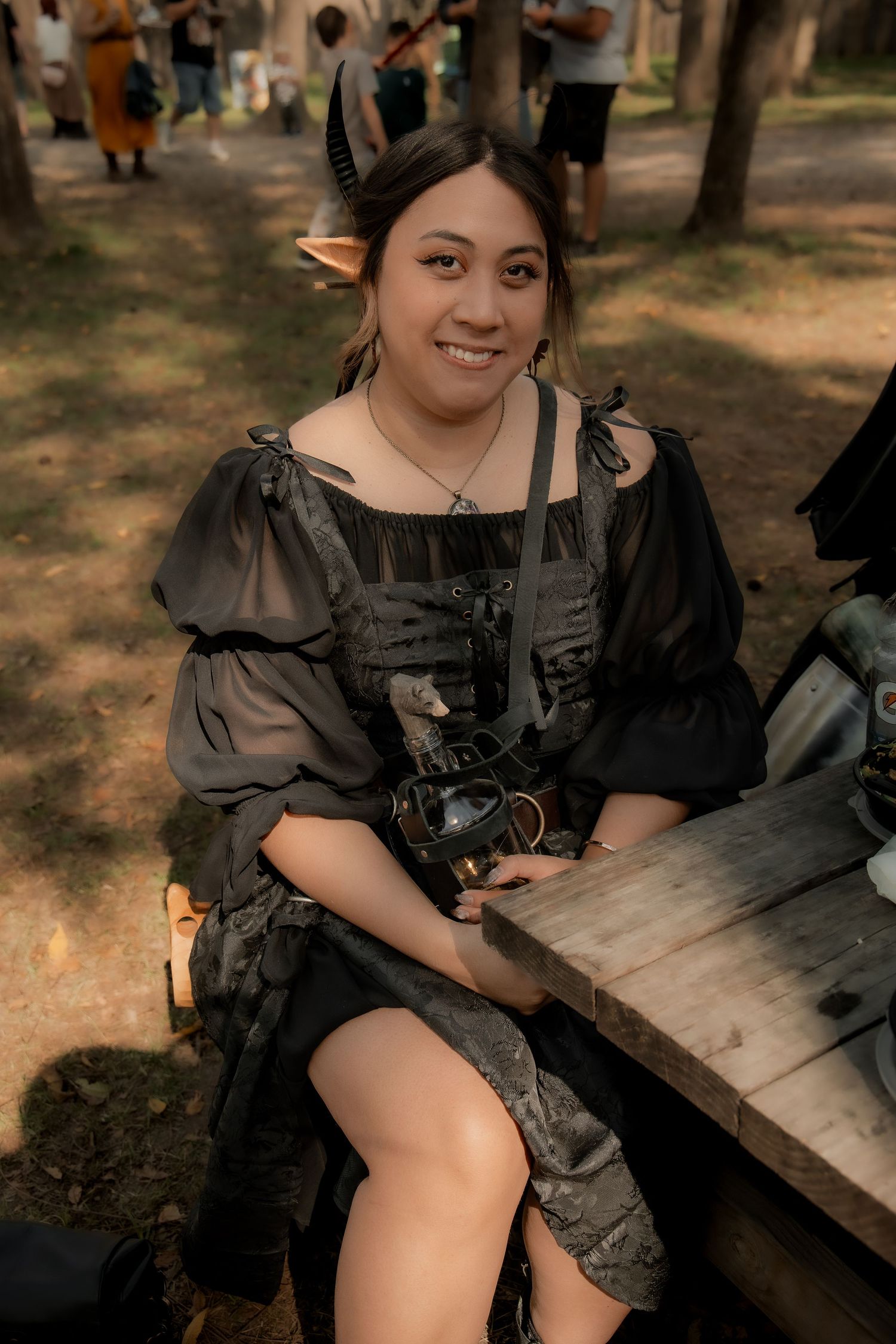 Person in a dark medieval costume sitting on a rustic wooden bench in a forest setting.