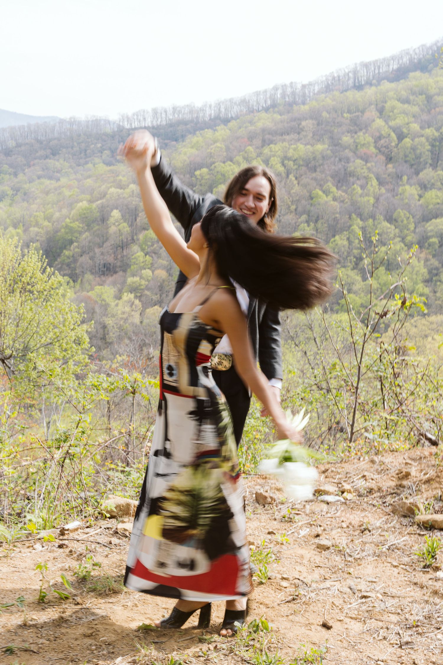 Joyful couple dancing and spinning outdoors on a mountain trail with blurred motion capturing their energy.