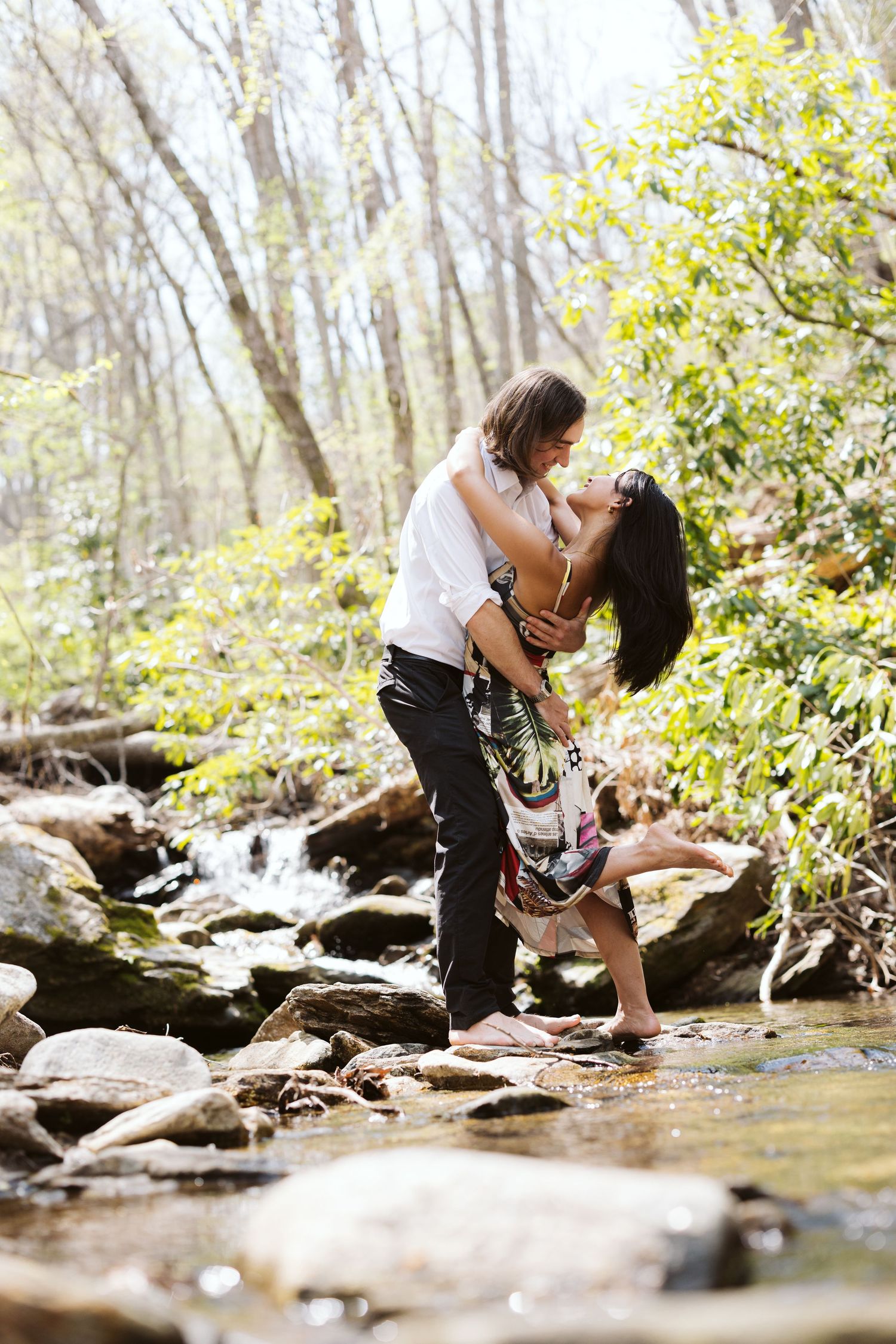 Romantic couple kissing while standing barefoot in a forest creek among rocks.