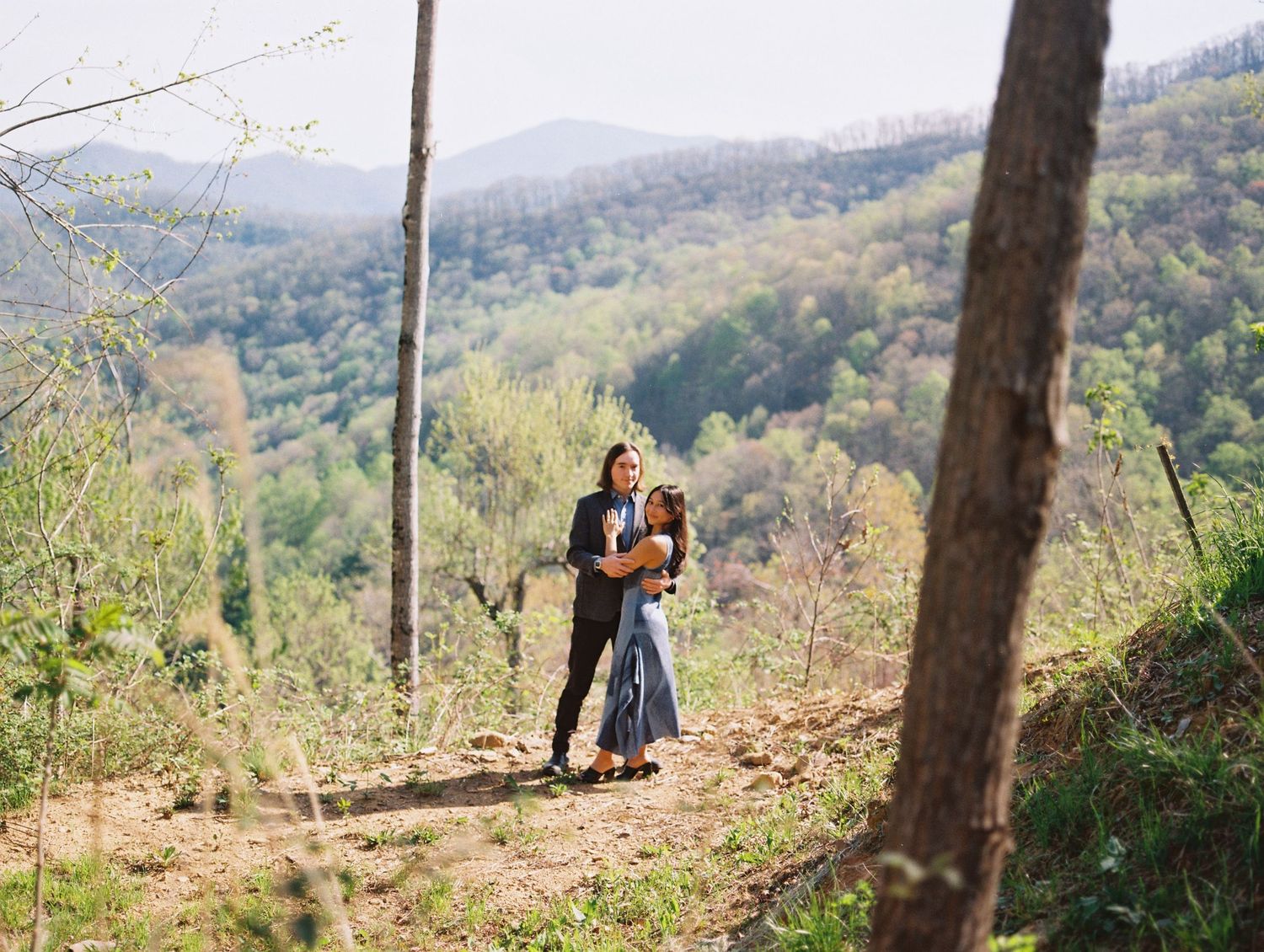 Couple embracing on a hilltop overlooking a lush green mountain valley landscape.
