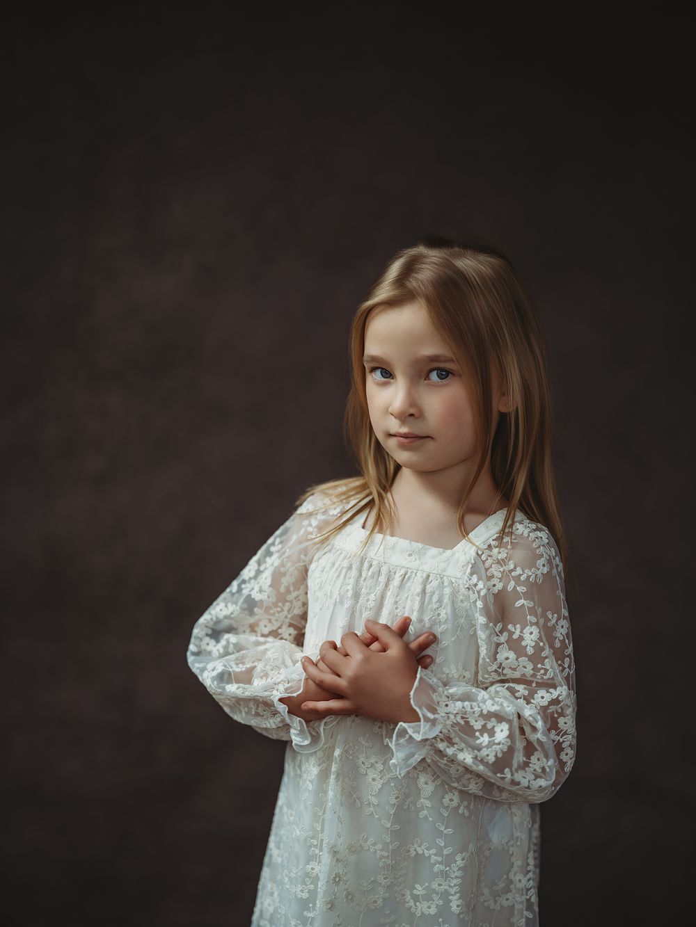 A series of artistic portrait photographs showing a child in a white lace dress against a dark background.