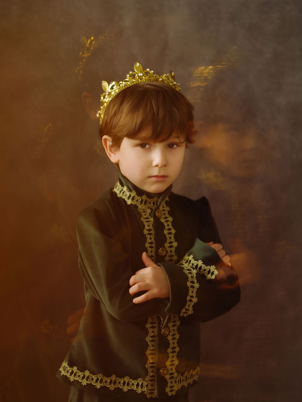 Young boy dressed as a royal king wearing a gold crown and dark ornate jacket in a vintage portrait.